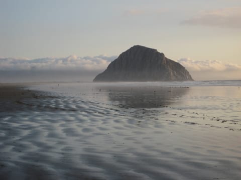 Morro Rock reflected in rippled wet sand and backed by fluffy white clouds on a dreamy evening.