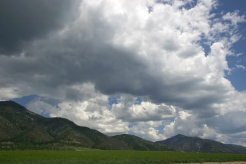 A sky full of clouds threatens to rain on hills and a green plain. 