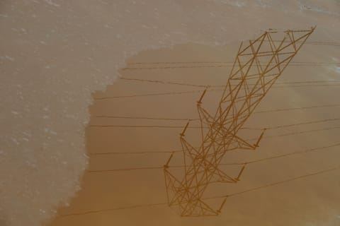 High voltage tower reflected in the water of a pink salt marsh. 