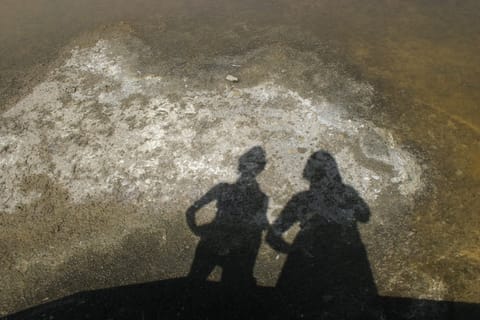 Two people cast shadows onto shallow water at the Alviso salt marshes.