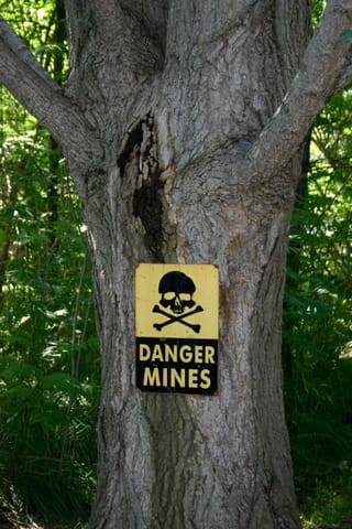 Yellow and black warning sign with a skull and crossbones that says, "DANGER. MINES."