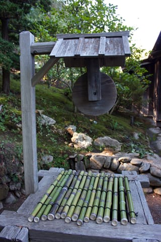 An old wooden water well in a Japanese garden, covered by bamboo stalks strung together. 